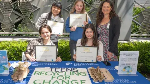 Four teen volunteers hold up their certificates next to librarian