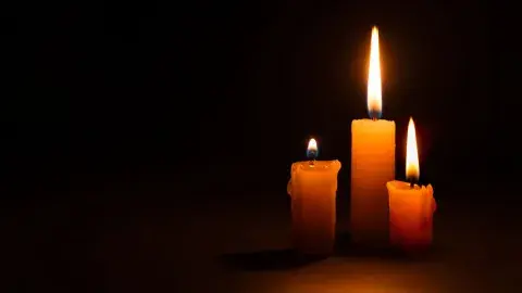Three burning taper candles against a black background.