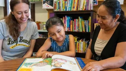 Two adults reading a book to a child. 