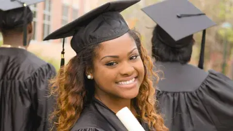 graduate in cap and gown, holding a diploma