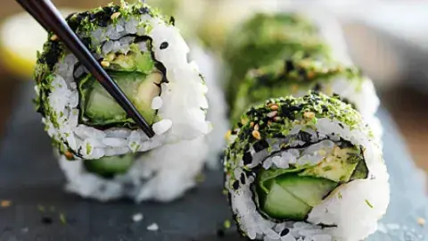 Close up photo of vegan sushi rolls. One piece is being picked up by chopsticks.