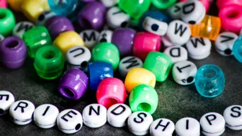 Image of white letter and multi colored beads. 