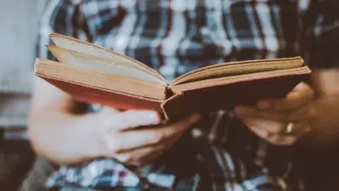 Man holding a book while wearing a plaid shirt