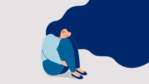 The image depicts a woman sitting on the floor with her knees tucked up towards her chest. She appears to be hugging her knees and her face is resting on them, suggesting a feeling of sadness, stress, or introspection. The image has white, light grey, and different shades of blue. her dark blue hair flows widely around her, taking up a significant portion of hte image.