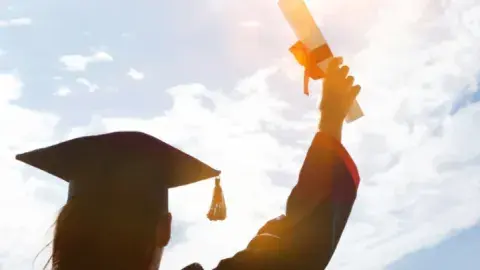 Shadow of a person holding up a diploma and wearing a cap and gown