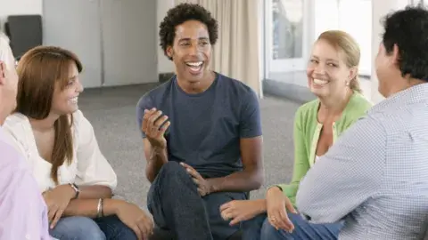 Group of adults sitting in chairs in a circle having a casual conversation and smiling