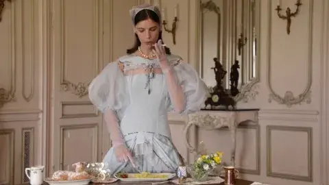 woman in gown smokes a cigarette while spooning mashed potatoes