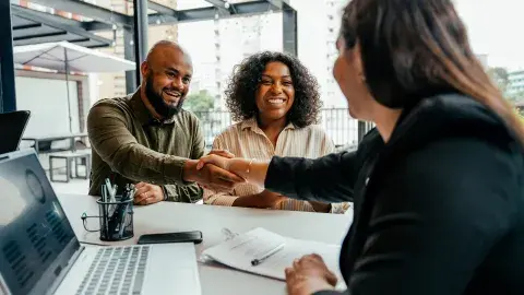 couple shakes hands with woman with laptop