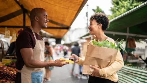 woman carrying paper bag of produce pays vendor