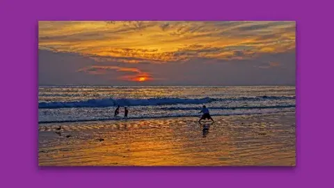 Three kids playing in the surf at sunset.