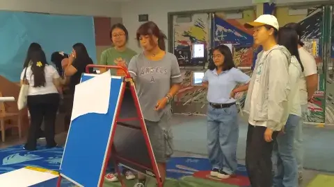 Group of teens stand in a circle around an easel to plan a program. 