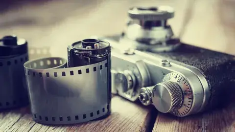 Close up photo of a camera and two rolls of 35mm film on a wooden surface.