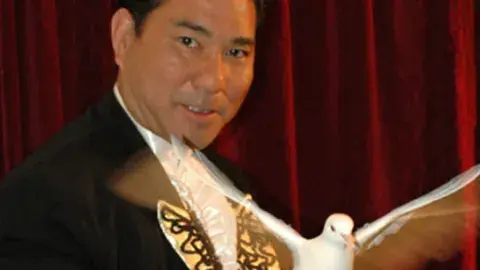 A magician holds a dove with wings outstretched.