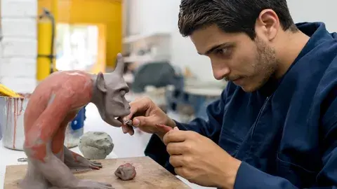 adult male making a gray and brown art figure out of clay