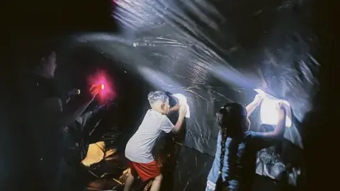 Two kids holding paper up to the sides of the black plastic wall of the planetarium while an adult shines a flashlight so they can see