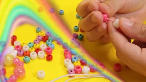 A pair of hands strings together a necklace of glittery, pink beads.