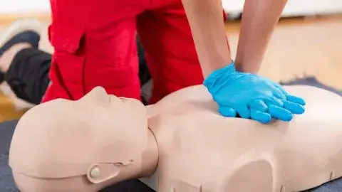 image of a person wearing blue gloves performing hands-only CPR on a mannequin