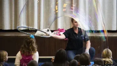 A Bubblologist makes a huge bubble in front of children.