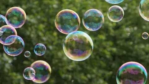 bubbles floating through the air in front of greenery