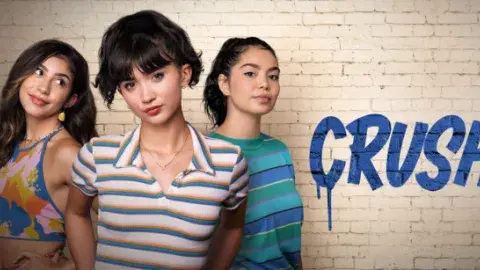 Three young women stand confidently against a white brick wall. The word "CRUSH" is painted in bold, blue letters. 