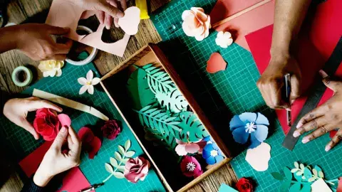 Three pairs of hands use crafting tools to make paper flowers.