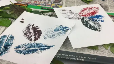 Pieces of paper with colorful images of leaves, actual leaves, and crayons, on top of pieces of newspaper