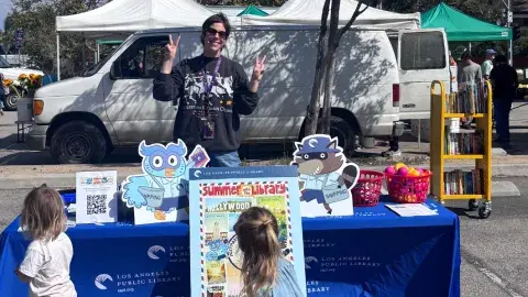 A librarian stands at a table at the Farmer's Market