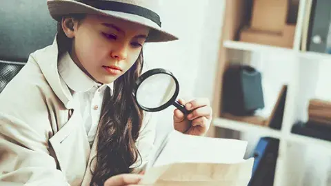 Girl in a trench coat and fedora looking through a magnifying glass