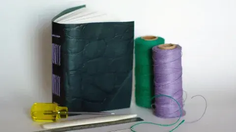 small book with a leather cover next to two spools of thread and other tools