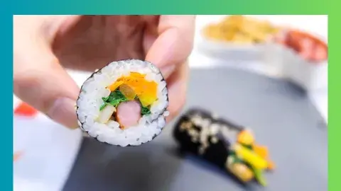 A hand grabbing a slice of mini kimbap and a out of focus roll in the background