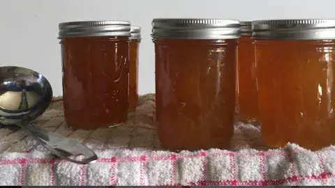 a spoon and four jars of jam atop a plaid tablecloth 