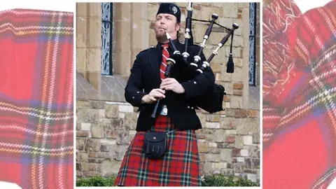 A man wearing scottish regalia is holding a bagpipe and blowing into a tube