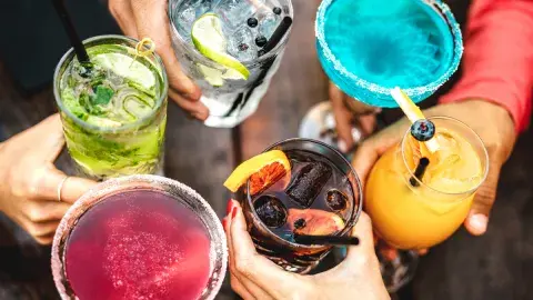 A group of people hold brightly colored drinks together