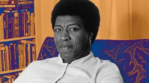 Author Octavia E. Butler sitting on a chair in front of a bookshelf