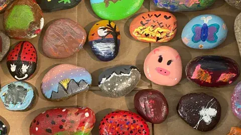 Colorfully painted rocks featuring animals, sunsets, butterflies, and abstract designs displayed on a table.