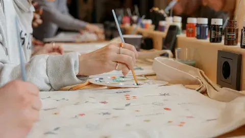 a woman is painting on a tote bag