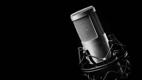 A closeup of a podcasting microphone against a black background.