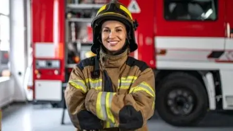 Female firefighter smiling in front of firetruck. 