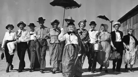 Historic photo of group of people carrying parasols or wearing hats, 1948.