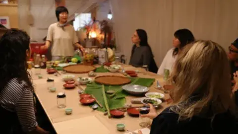 Jessica Wang giving a food preparation demo to people seated around a table.