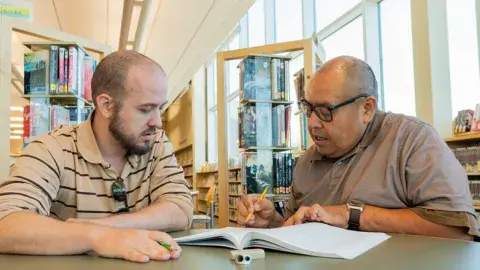 A tutor with a learner reviewing a book.