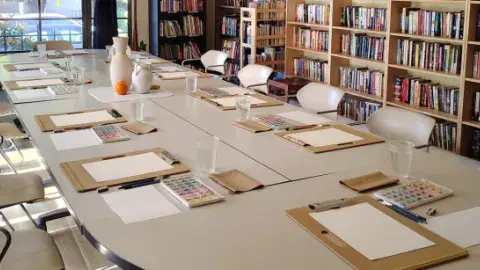 Room prepared for an art program with boards, papers, watercolors and a still life with three vases in the center