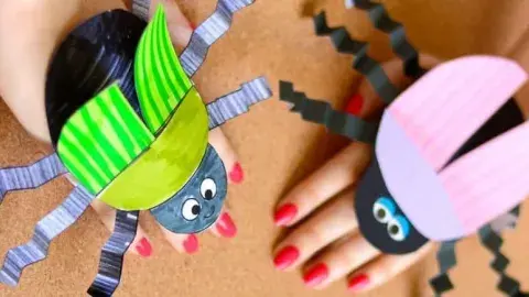 Beetle crafts, wrapped around hands, created with black, pink and green paper.
