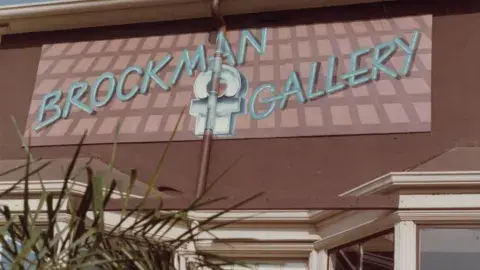 "Brockman Gallery" sign painted in blue over pink background