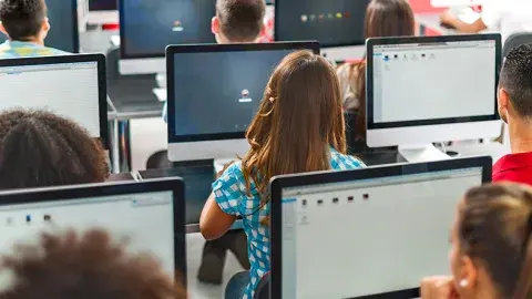 several students sitting at computer in a class room, seen from the back of the room
