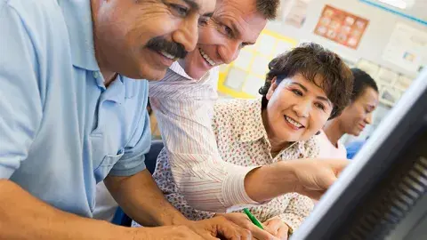 A group of adults looks at a computer screen, smiling and gesturing.