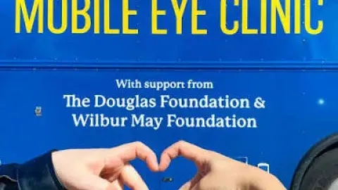 Two hands forming a heart in front of the "Mobile Eye Clinic" vehicle.