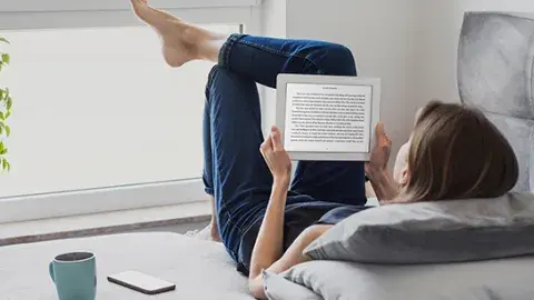 A girl reads on her tablet in front of a sunny window