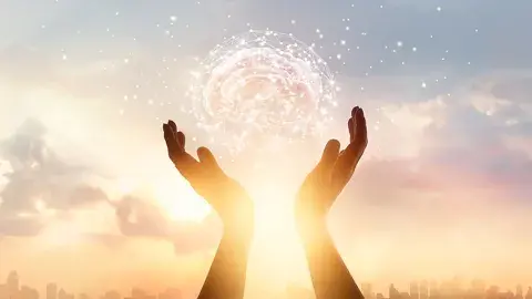 Two hands backlit by sunlight, holding a glowing brain aloft, representing creativity.