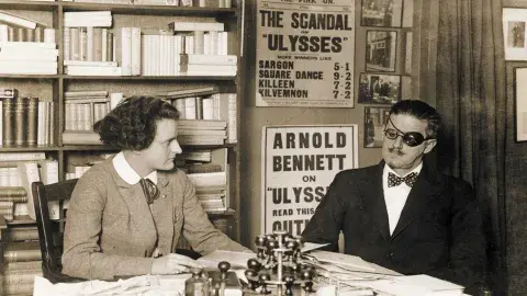 James Joyce with Sylvia Beach sitting next to each other at a desk.